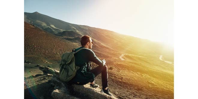 Man with rucksack sitting on rock at sunset on volcano Etna mountain in Sicily Free Photo