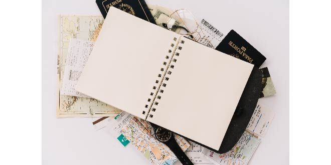 Elevated view of blank spiral notebook on passports and maps against white background Free Photo